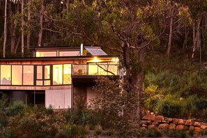 A modern house with large windows, a solar panel, and a stone wall.