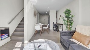A modern living room with a grey sofa, a coffee table, and a staircase leading to a dining area with white chairs and a small table. - Chic 1-bed loft in Playhouse square, near Stadiums, Theater, Dining, Pets OK (Cleveland)