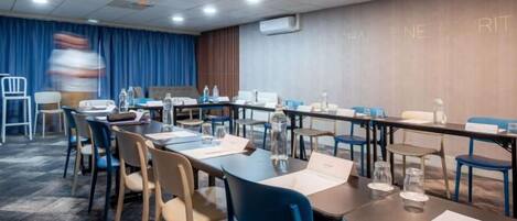 A conference room with tables, chairs, and a blue curtain backdrop.