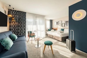 Une chambre d’hôtel moderne avec un canapé, un lit, une petite table et une valise.