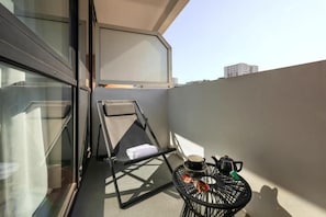 A balcony with a folding chair, a small table with a kettle, and a window. - Mercure Paris Montparnasse Pasteur (Paris)