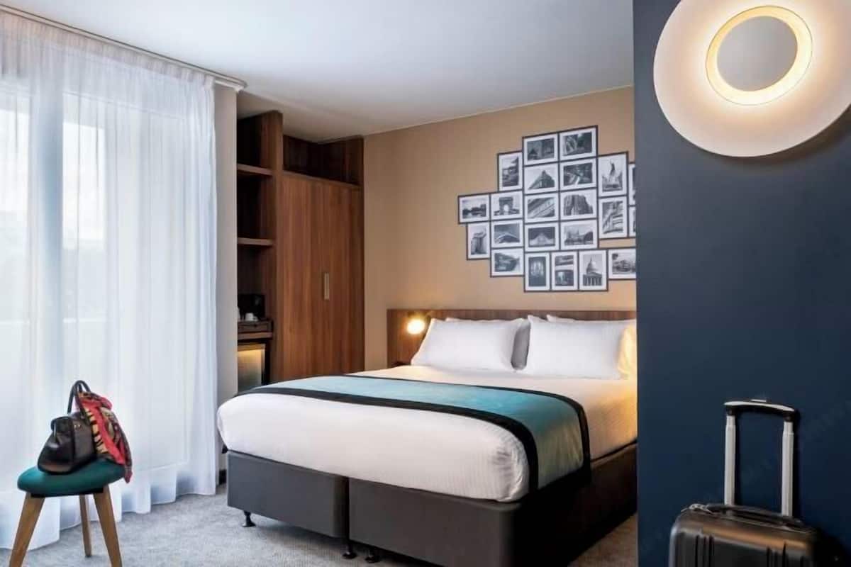A hotel room with a bed, a wall-mounted picture gallery, a suitcase, and a chair with a bag.