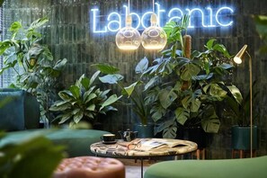 A cozy indoor space with a neon sign, potted plants, and a round table with a lamp. - Mercure Paris Montparnasse Pasteur (Paris)