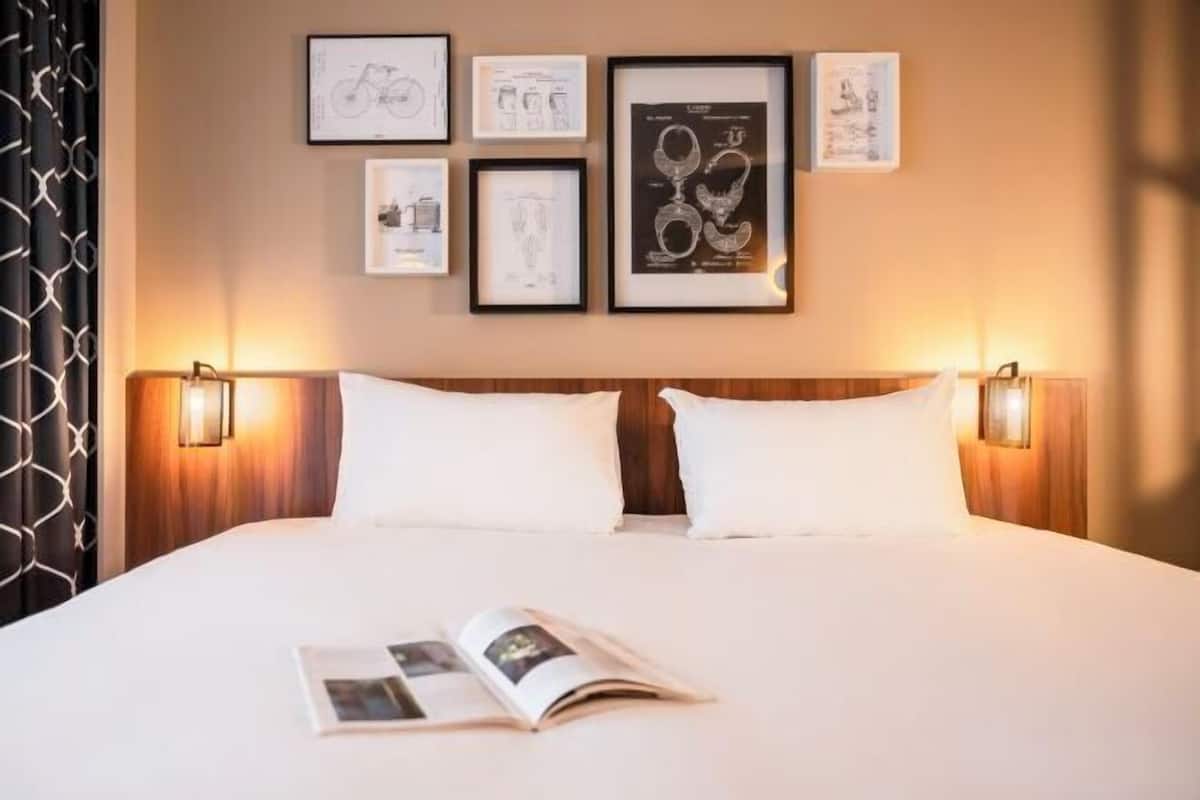 Une chambre d’hôtel avec un grand lit, deux lampes de chevet et des œuvres d’art encadrées accrochées au mur.