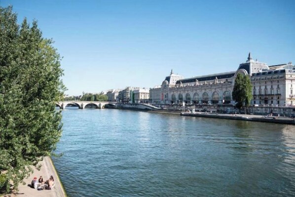A river with a bridge, a large building with arches, and a tree-lined promenade. - Mercure Paris Montparnasse Pasteur (Paris)