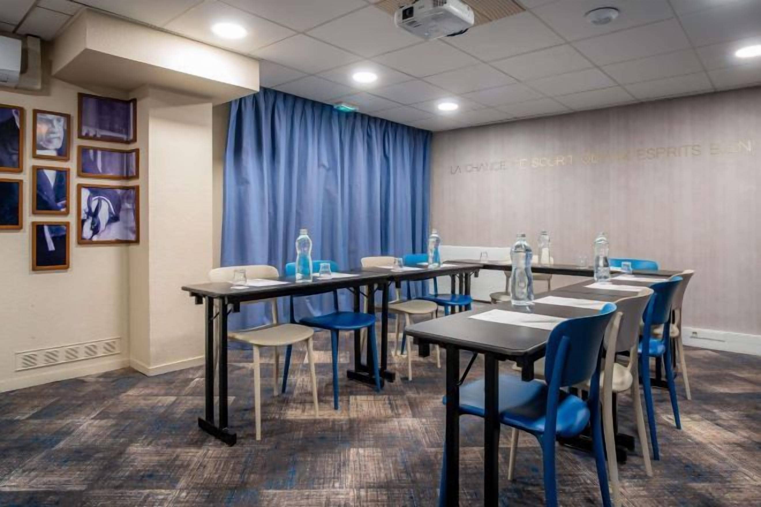 Une salle de conférence équipée de tables et de chaises, d’un projecteur et d’un rideau bleu.
