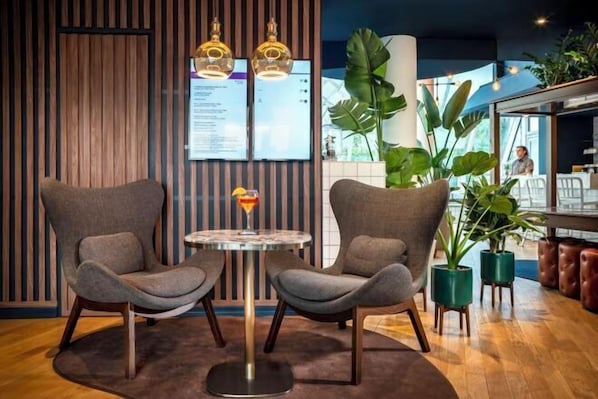 Un intérieur moderne avec deux fauteuils gris, une table ronde sur laquelle se trouve une boisson et un panneau affichant le menu.