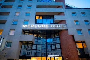 El exterior del hotel Mercure, con un letrero llamativo, fachada de vidrio y detalles en ladrillo.