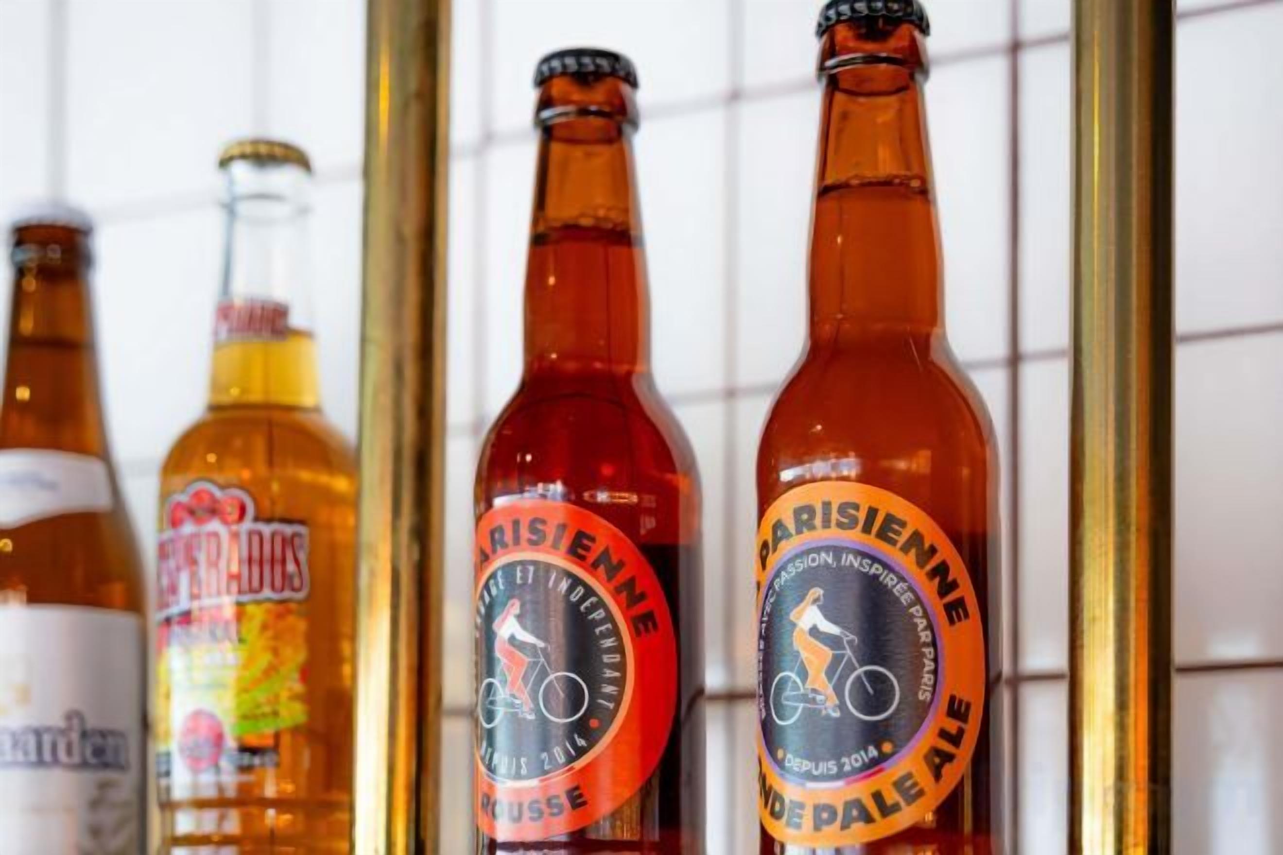 Quattro bottiglie di birra con etichette, disposte in fila su un muro piastrellato.
