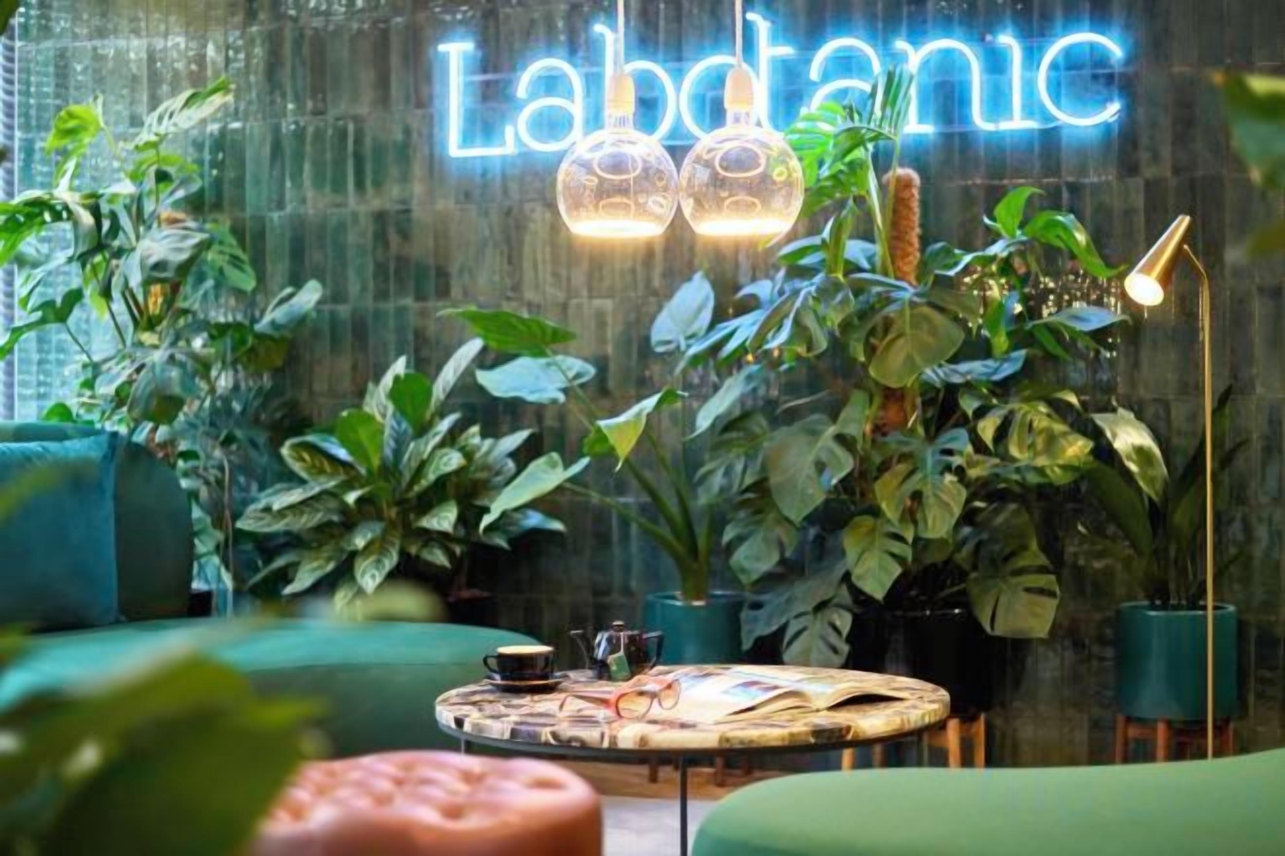 A cozy indoor space with a neon sign, green seating, and various plants.