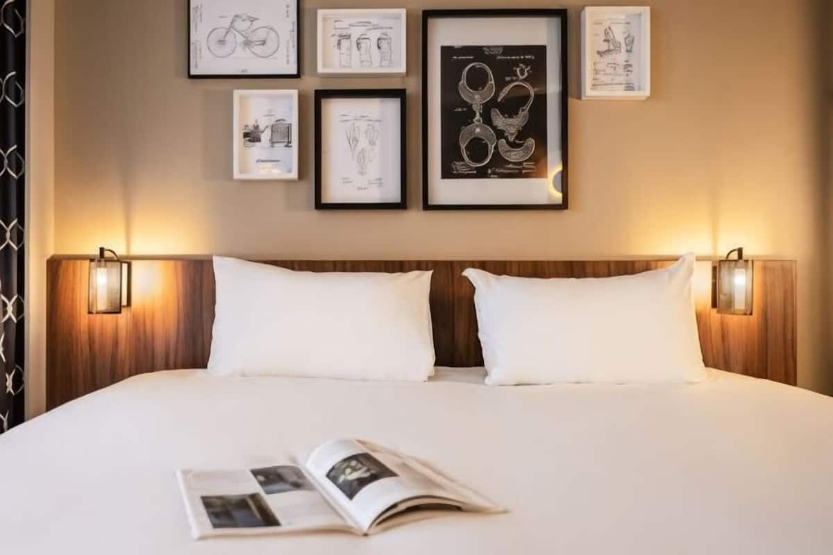 A neatly made bed with white linens, a book on the bed, and framed artwork on the wall.