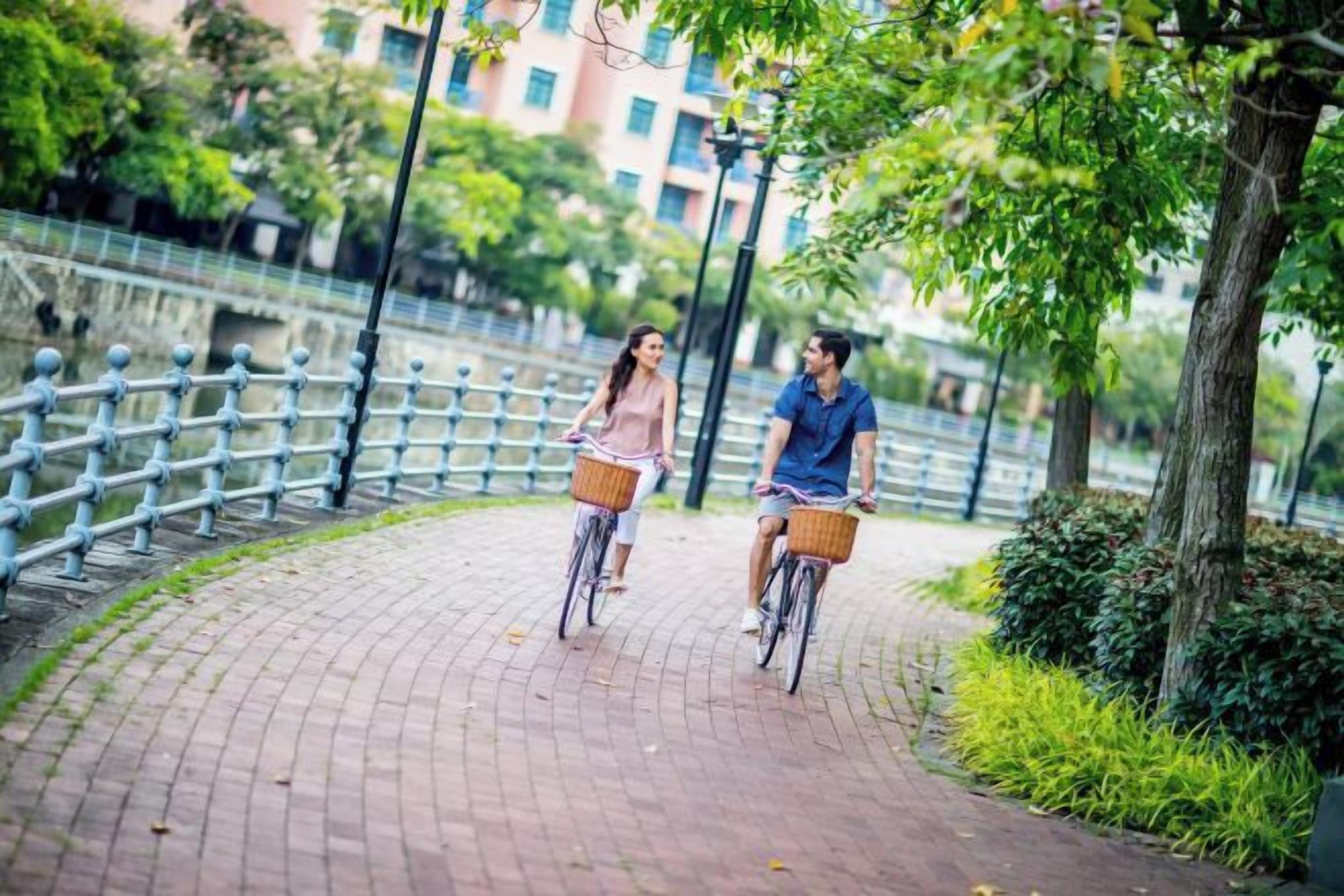 Dos personas andando en bicicleta por un camino pavimentado con barandillas metálicas a un lado.