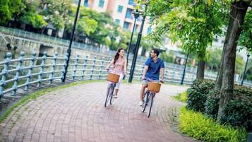 Dos personas andando en bicicleta por un camino pavimentado con barandillas metálicas a un lado.