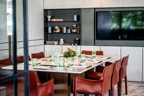 Un comedor con una mesa larga, sillas rojas y un televisor montado en la pared.