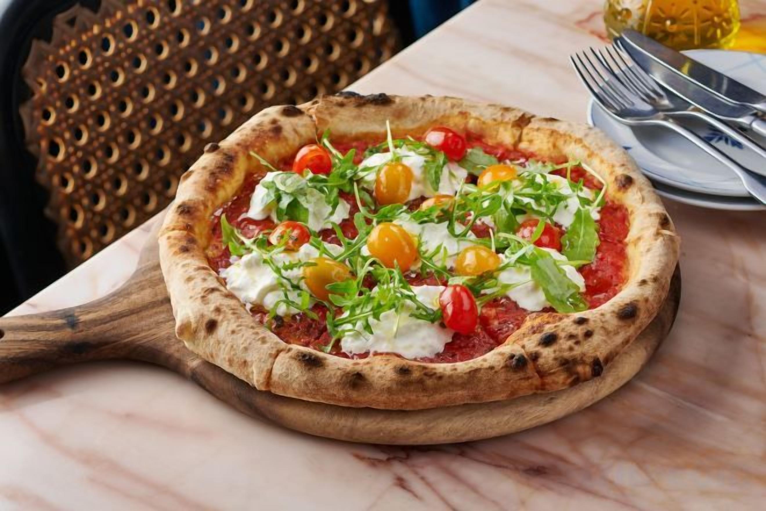 Una pizza sobre una tabla de madera, con una mesa de mármol y una silla decorativa al fondo.