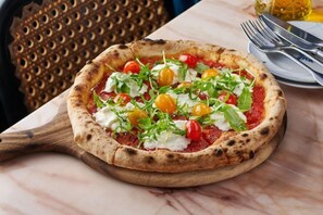 Una pizza sobre una tabla de madera, con una mesa de mármol y una silla decorativa al fondo.