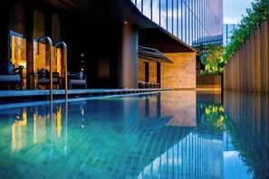 Una piscina interior moderna con agua cristalina, sillones de descanso y vistas a un paisaje urbano.