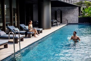 Zona de piscina con sillones de descanso y una persona nadando.