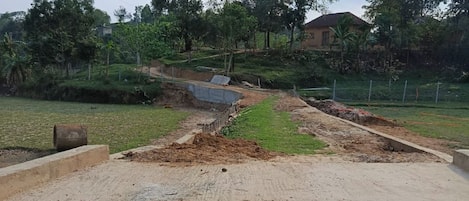 Un cantiere con terreno nudo, strutture in cemento e una zona verde alberata sullo sfondo.