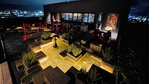 A rooftop bar with outdoor seating, a red railing, and a view of the city at night. - Núcleo Sabana, San José, Apartment with A/C, 20 minutes from the Airport (San José)