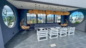 A modern outdoor seating area with a sofa and chairs, large windows offering city views, and a ceiling with hanging wicker lamps. - Núcleo Sabana, San José, Apartment with A/C, 20 minutes from the Airport (San José)