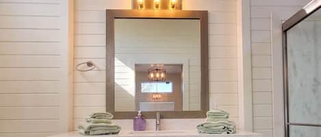 A bathroom with a large mirror, a sink, a towel rack, and a shower area.
