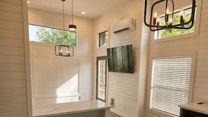 A bedroom with a built-in window seat, a bed, a TV, and an air conditioning unit. - Turquoise Triangle Tiny Homes (Cottonwood)