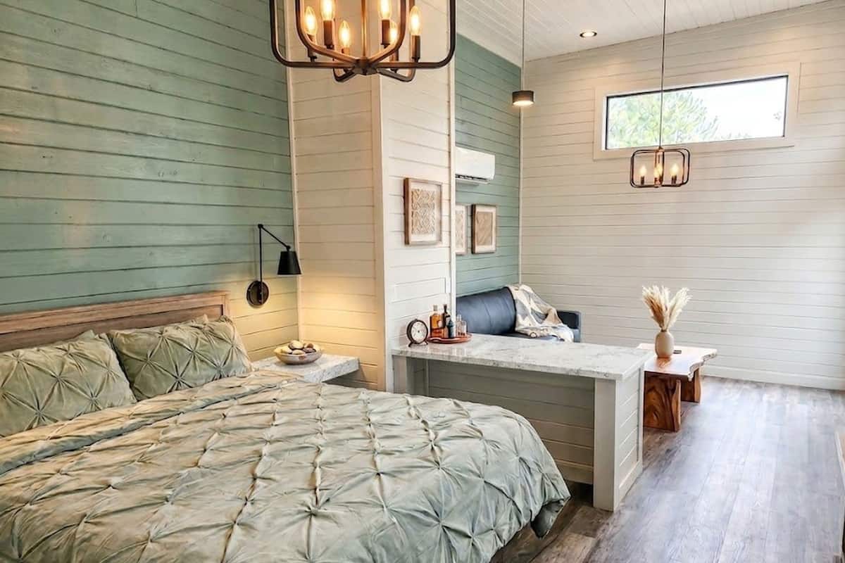 A bedroom with a bed, a desk, a chair, a lamp, and a window.