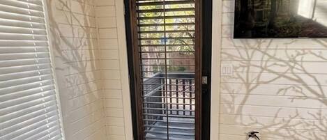 Una habitación con suelo de madera, una puerta enmarcada en negro con un ventanal, una lámpara en el techo y un extintor.