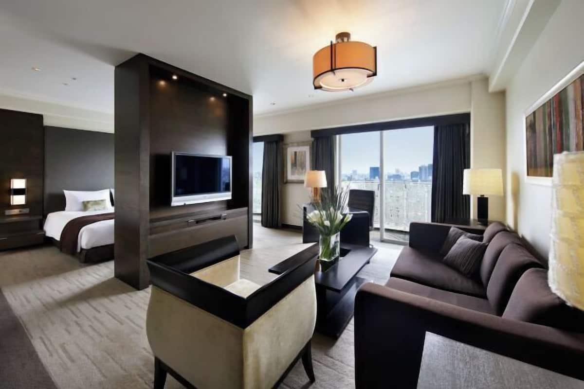 Una habitación de hotel con cama, televisión, escritorio, sofá y un amplio ventanal con vista a la ciudad.