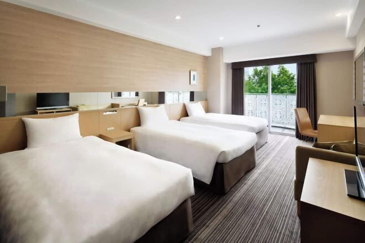 Una habitación de hotel con tres camas, un escritorio, televisión y balcón con vistas.