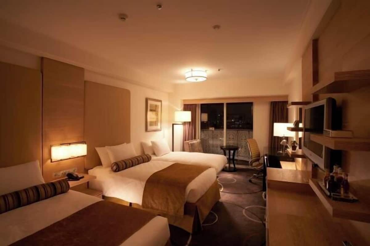 Habitación de hotel con dos camas, un escritorio, una silla, un televisor y un balcón con vistas.