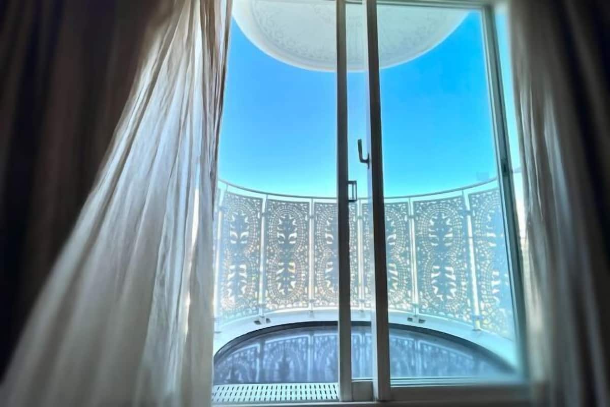 Un balcón con elaborada barandilla de celosía y un cielo azul despejado.