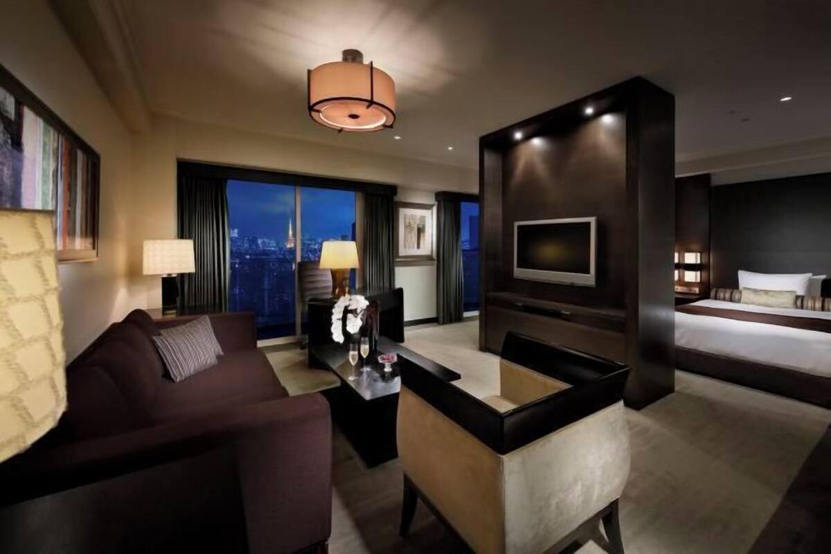 Una habitación de hotel moderna con una cama grande, un sofá, una mesa de centro, un televisor y vistas a la ciudad.