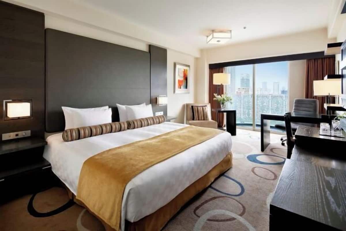 Habitación de hotel con una cama grande, un escritorio y vistas a la ciudad.