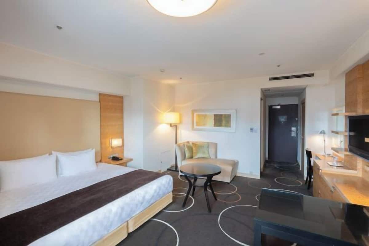 Una habitación de hotel con cama, escritorio, silla, lámpara y televisión.