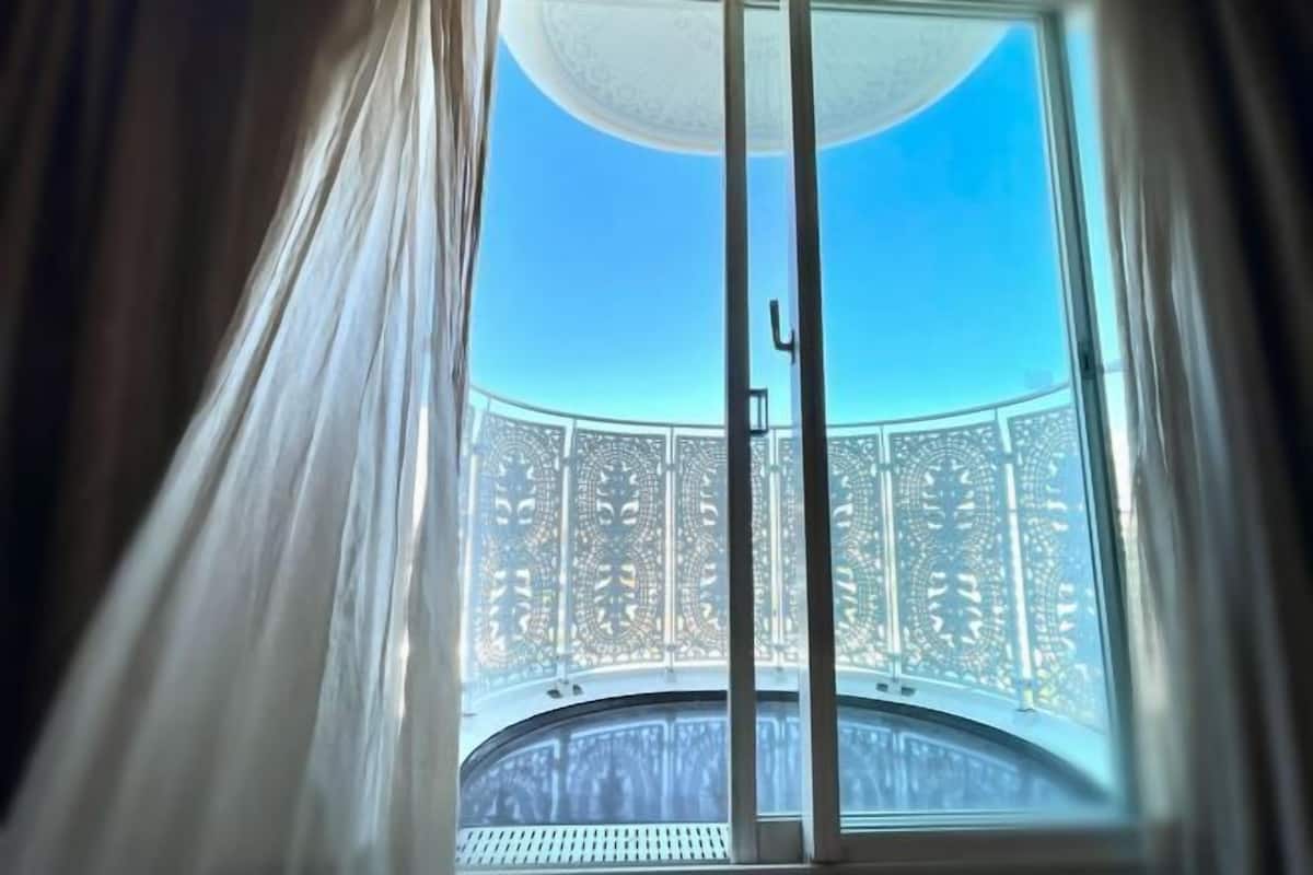 Una habitación con un ventanal grande, una puerta corredera y vistas a un balcón con barandilla ornamental.