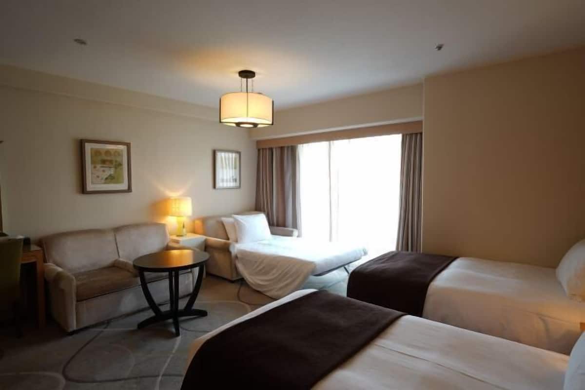 Habitación de hotel con sofá, una mesita redonda, cama y un ventanal con cortinas.