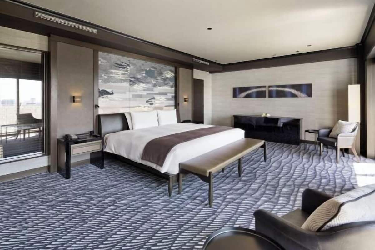 Una habitación de hotel moderna con una cama grande, un banco, una zona de estar y vistas a la ciudad.