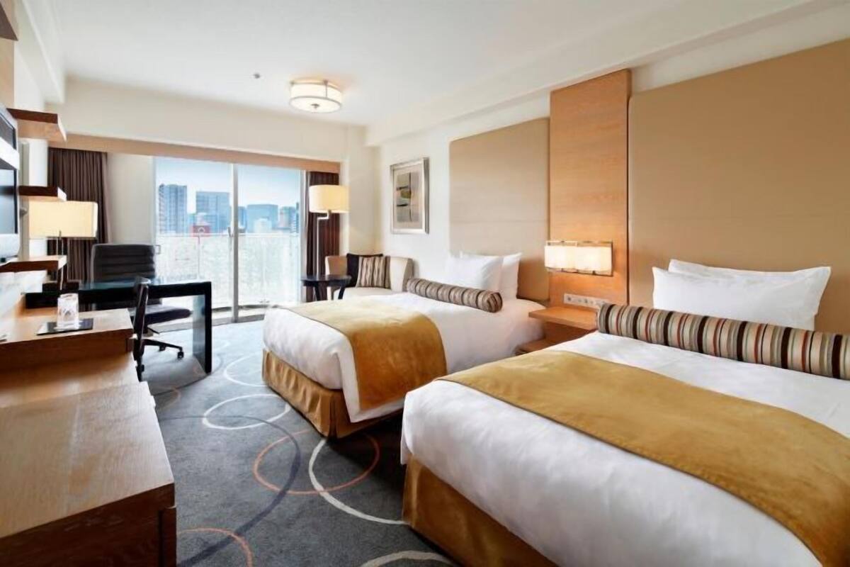 Habitación de hotel con dos camas, un escritorio, una silla y vistas a la ciudad.