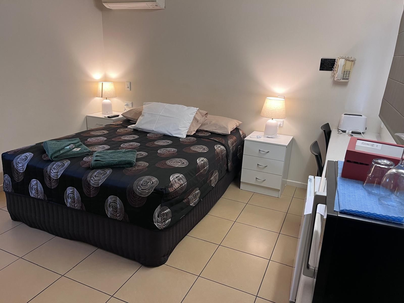 Une chambre d’hôtel comprenant un lit, des tables de chevet, un bureau, une chaise et un réfrigérateur.