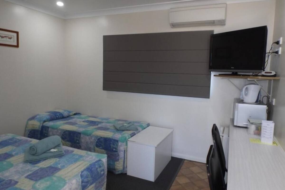 A room with two beds, a desk, a chair, a television, and a microwave.