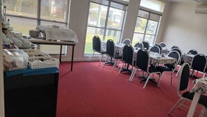 A conference room with tables and chairs, a buffet area with food items, and large windows providing a view of the outdoors. - THREE MOON MOTEL (Monto)