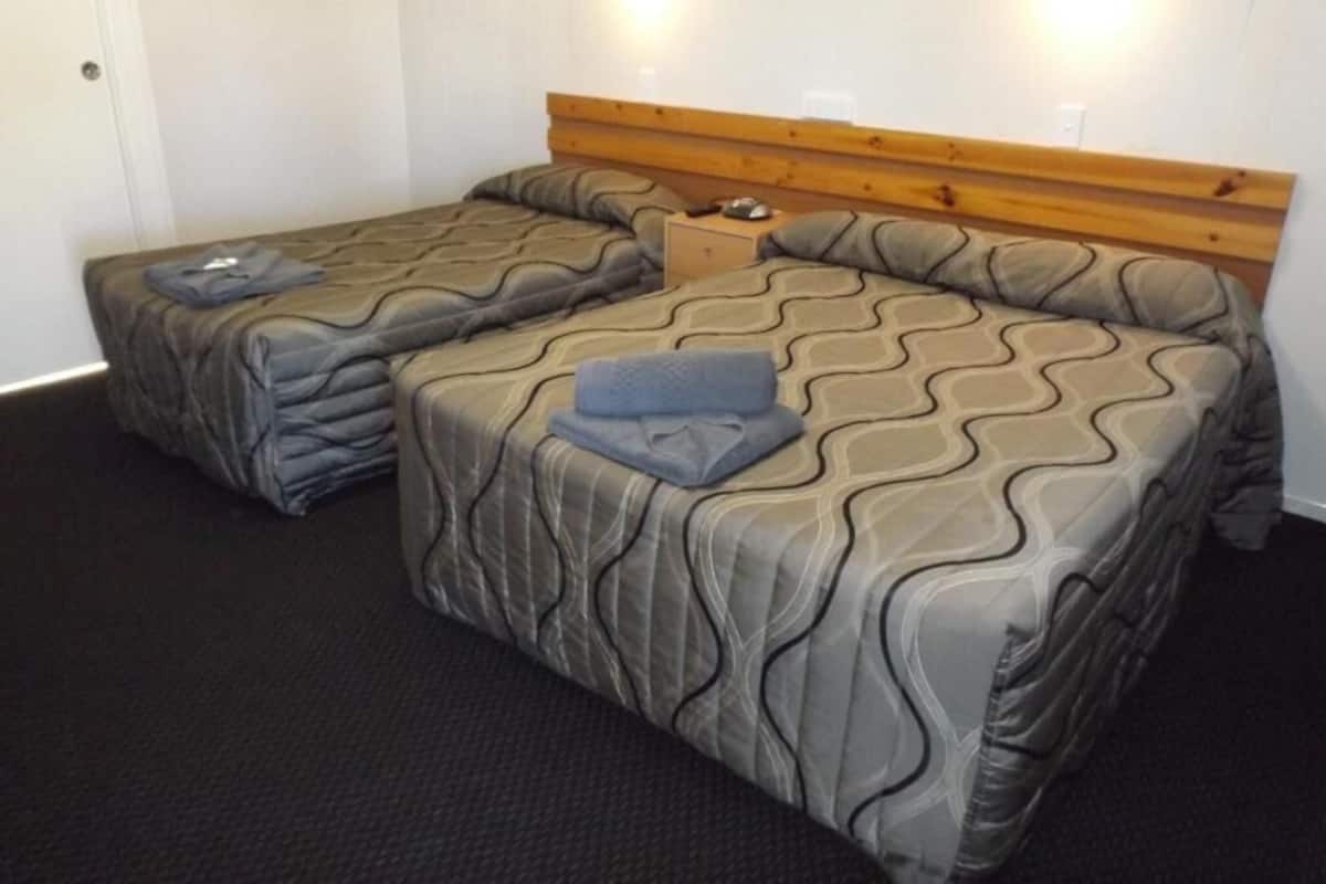 A room with two beds, each with a wooden headboard and grey patterned bedding.