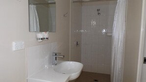 A bathroom with a sink, mirror, shower, and tiled walls. - THREE MOON MOTEL (Monto)