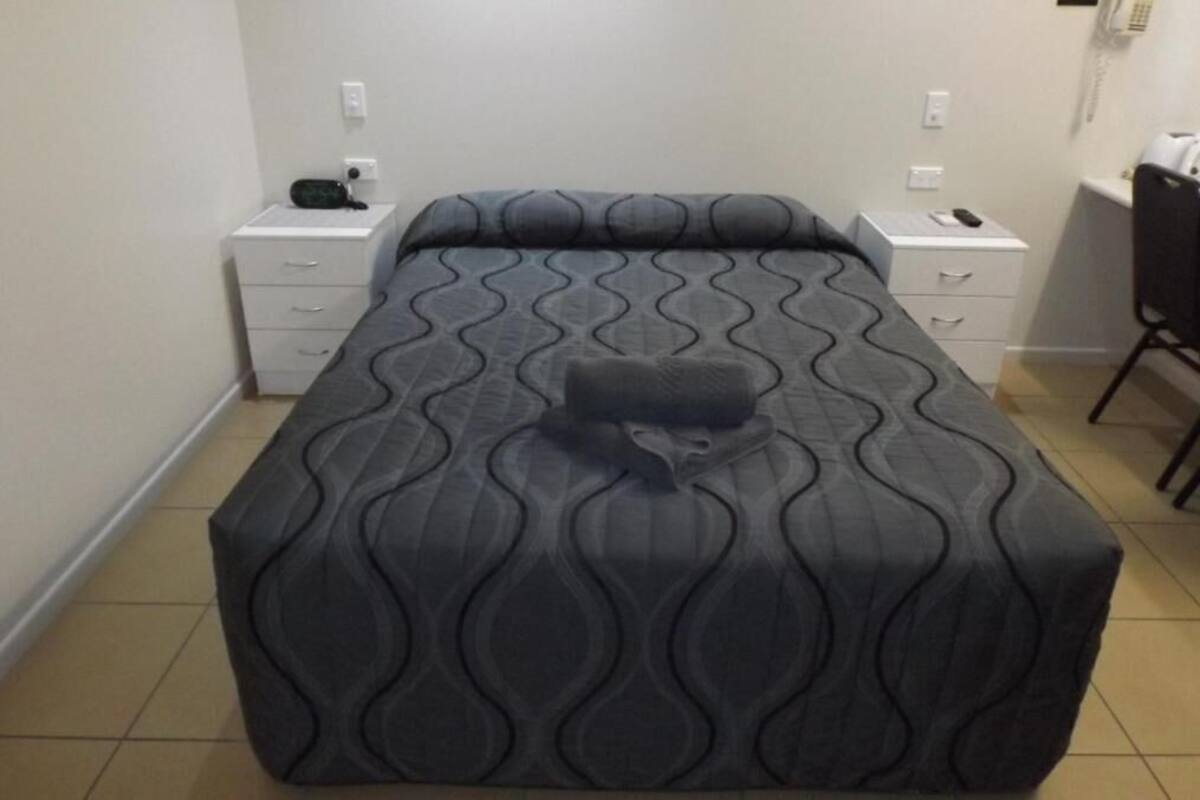 A neatly made bed with a patterned bedspread, two bedside tables with drawers, a chair, and a phone on one of the tables.