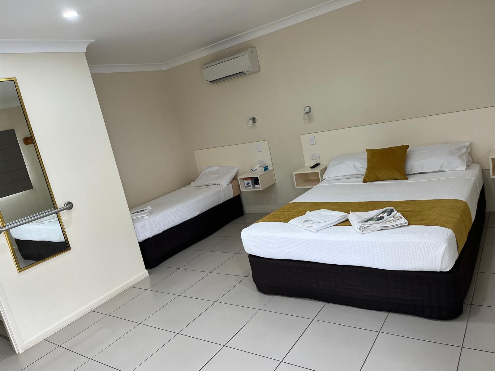 Ein Hotelzimmer mit zwei Betten, einem Spiegel, einem Nachttisch und einer Klimaanlage.