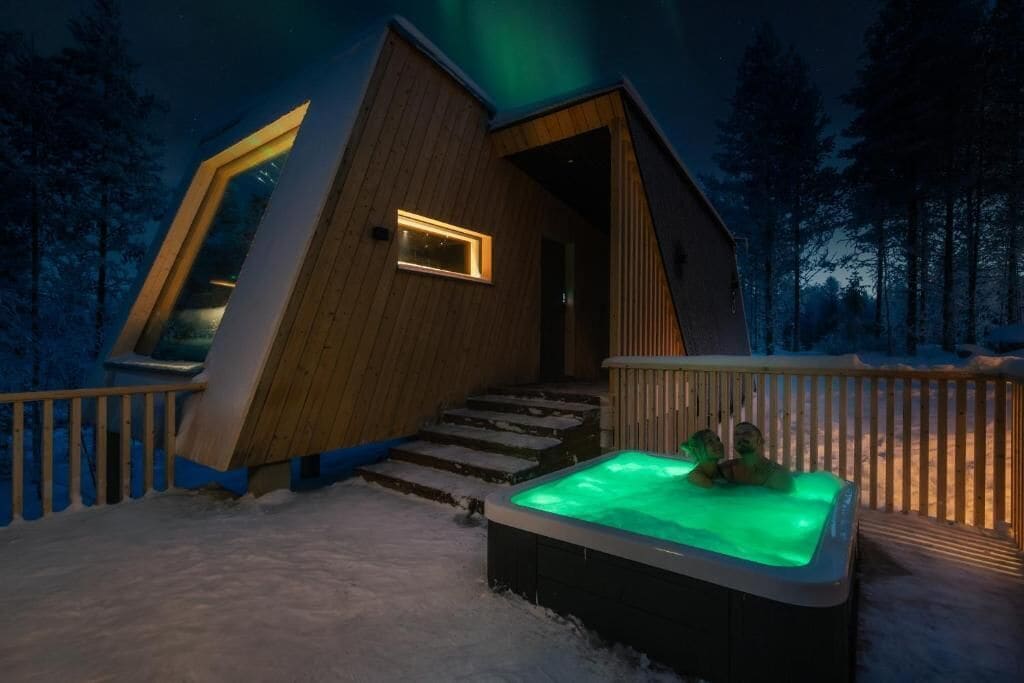 A modern wooden cabin with a unique sloped roof design, a hot tub, and a wooden deck.