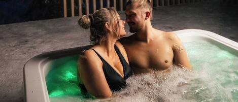 A couple in a hot tub with a snowy forest backdrop.