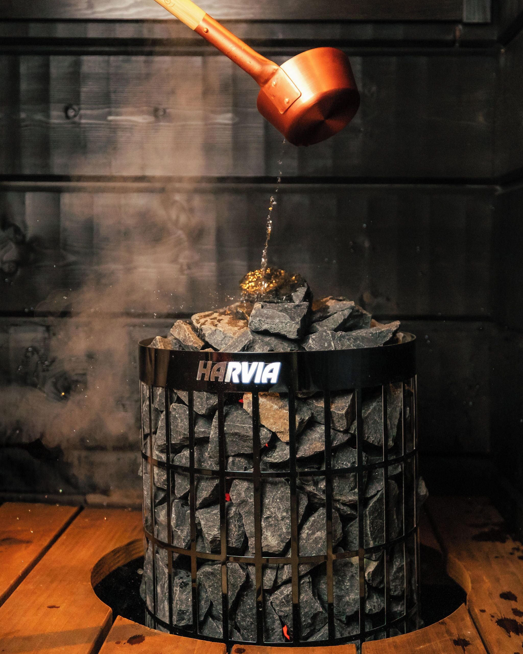 A charcoal grill with a metal grate labeled "HARVIA" being filled with charcoal.